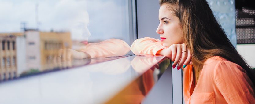 Een vrouw leunt op een kozijn, denkt na en kijkt uit het raam
