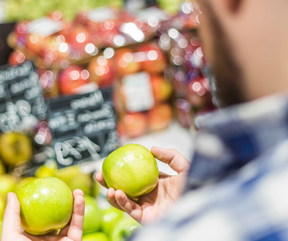 Een man die twee appels vergelijkt, in de supermarkt bij de fruitafdeling